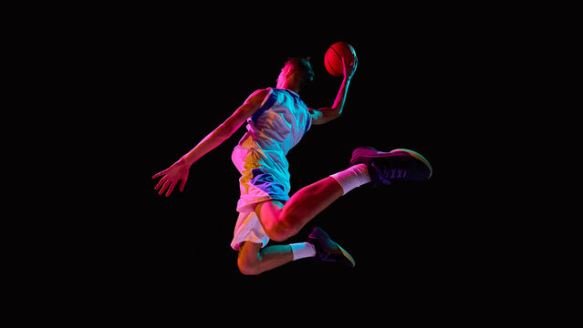 Basketball player soaring with ball in neon lights showing athletic power. Concept of sports advertising, youth lifestyle branding, motivational design, and digital campaigns.