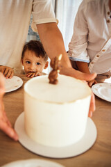 Young boy eagerly watches as an adult places a beautifully decorated cake on a table, surrounded by family members, creating a joyful celebration atmosphere