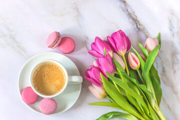 Top view for cup of coffee with macaroons and bouquet of pink tulips on a marbre background