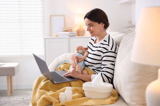 Telehealth. Smiling mother with her baby having online consultation with doctor by laptop on sofa at home
