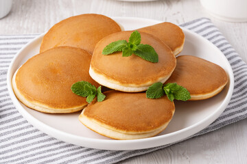 Fluffy pancakes stacked on a white plate with fresh mint leaves on a gray striped cloth