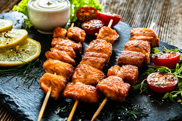 Fried salmon skewers with white dip on stone board on wooden table	