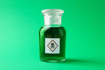 Bottle of poison with warning sign on green background, closeup