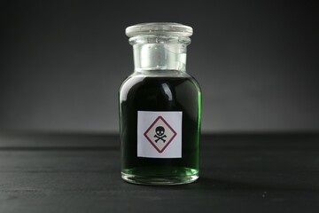 Bottle of poison with warning sign on black wooden table, closeup