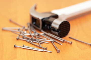 A hammer lies on a pile of construction nails on a wooden table, symbolizing manual labor and tools for construction and repair