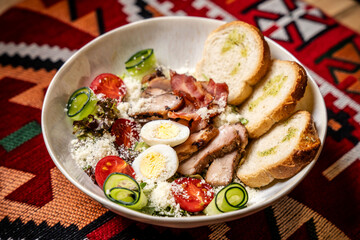 Caesar salad with chicken, eggs and bread on ethnic background