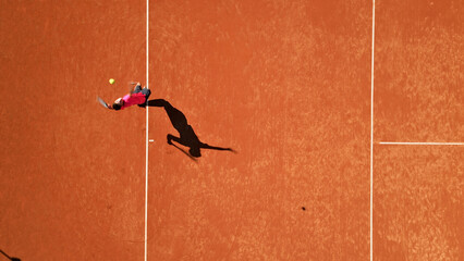 Tennis player in red shirt and black shorts stretches dynamically on a clay court, showcasing focus and agility. Aerial shot highlights sports training and skill development in a sunlit setting. © stockcopter