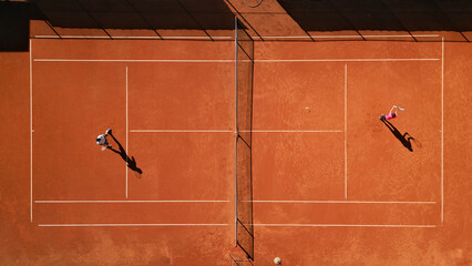 High-angle view of two athletes practicing on a clay tennis court, highlighting dynamic movement and focused training. The vibrant orange surface emphasizes dedication to skill development.