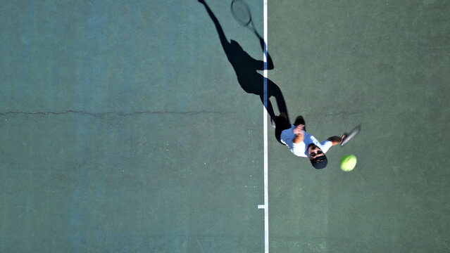 Tennis player on hardcourt executing forehand stroke. Overhead view captures dynamic motion and focused intensity, highlighting skill development and sports training dedication.