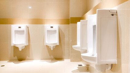 A row of white urinals in a modern public restroom, viewed from a side angle with neat tiled walls...