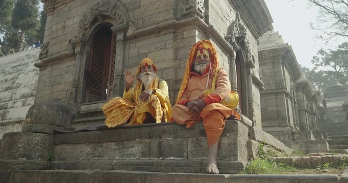 A Sadhu Yogi in yellow attire meditates with sacred hand mudras at Pashupatinath Temple, Kathmandu, Nepal. His devotion to the gods symbolizes Hindu spirituality, culture, and sacred tradition