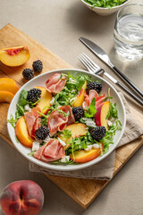 Fresh salad with peaches, arugula, feta, prosciutto and berries in a plate on a wooden board