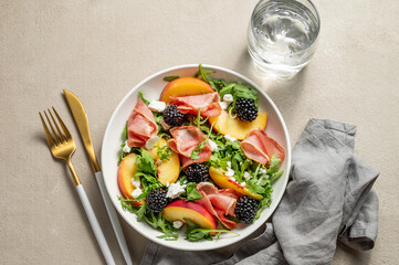 Fresh salad with peaches, arugula, feta, prosciutto and berries in a plate on a light background