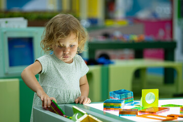 Cute toddler girl playing with colorful magnetic tiles on light table in playroom