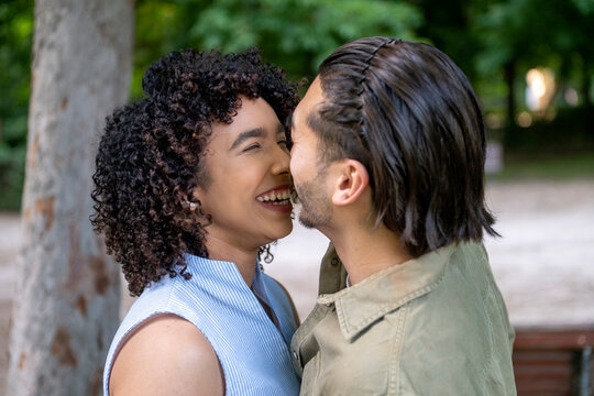 Happy interracial couple laughing and embracing in park - Powered by Adobe