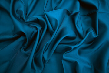Blue silk fabric with soft folds and drapery. Shiny textile texture creates a sense of elegance, luxury, and sophistication. Perfect as an abstract background for fashion projects or advertising.