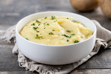 Mashed potatoes in white bowl on rustic wooden table