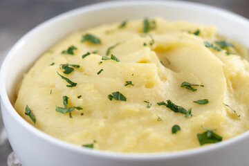 Mashed potatoes in white bowl on rustic wooden table. Close up