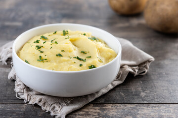 Mashed potatoes in white bowl on rustic wooden table. Copy space