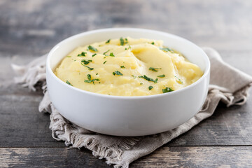 Mashed potatoes in white bowl on rustic wooden table