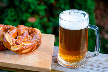 having beer and pretzel outdoors. celebrate oktoberfest. glass mug with cold beverage on the dark background of garden. rustic scene