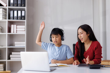 Asian child raising hand during online class with teacher assisting