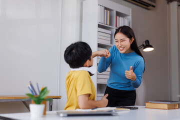 Asian teacher and student fist bumping in classroom, celebrating success and encouraging education