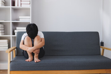 Sad child sitting on sofa hugging knees