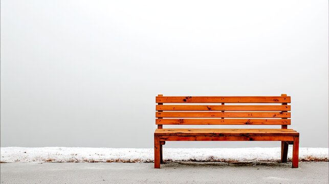 A weathered wooden park bench sits alone amidst a hazy, snowy landscape.