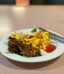 a dish of beef steak with French fries and tomato sauce on a plate at a buffet restaurant