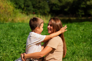 Fototapeta premium Portrait of young Caucasian single mother hugging her cute small son outside in park sending time on summer day together. Motherhood concept.
