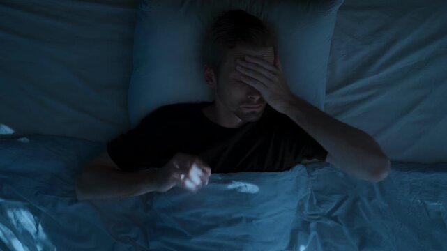 Top view, man restlessly sleeping in bed at night and waking up abruptly with a startle. Insomnia sleep paralysis, sleep disorder