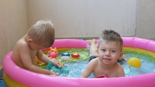 Happy children play in small pool, splashing water with joy. Smiling boys splash in the pool, enjoying refreshing water play. Kids enjoy sunny fun in the pool, their laughter echoing with water games