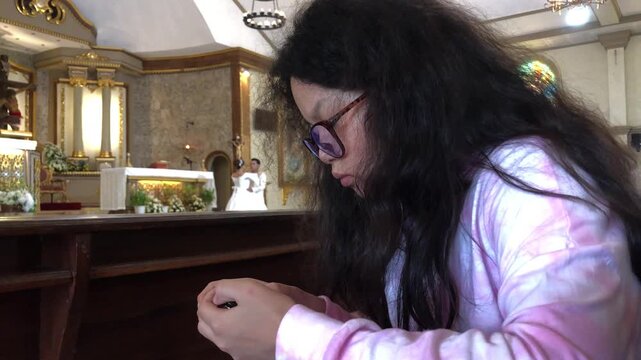Young Asian teen girl is deeply focused on playing mobile games in the church hall, unaware of her surroundings.