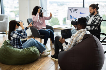 Group of diverse adults using virtual reality headsets and laptops in modern office setting. Individuals of various backgrounds collaborating in technology-driven workspace fostering creativity