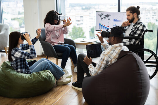 Group of diverse adults using virtual reality headsets and laptops in modern office setting. Individuals of various backgrounds collaborating in technology-driven workspace fostering creativity - Powered by Adobe