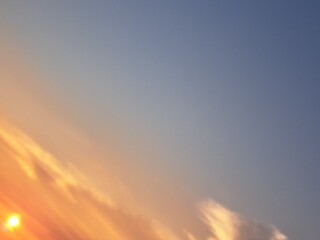Evening sunset with an orange blue sky – White and grey clouds illuminated by the last remaining rays of the bright orange evening sun, amidst a darkening blue sky.