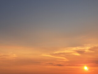 Evening sunset with an orange blue sky – White and grey clouds illuminated by the last remaining rays of the bright orange evening sun, amidst a darkening blue sky.