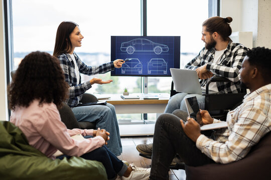 Engineers and designers brainstorming for new car design development using digital screen. Group of multicultural young adults engaged in collaborative teamwork session.