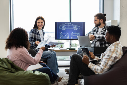 Collaborative team of diverse young professionals discussing car design project using laptop and documents