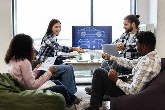 Creative designers working on vehicle concept, discussing plans, reviewing blueprints in workspace. Image shows diverse team including men and women, representing inclusive professional collaboration