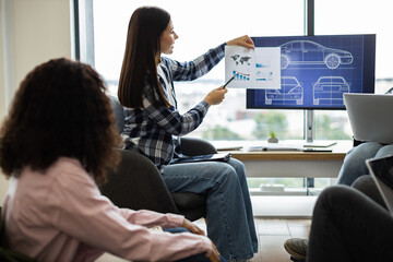 Business meeting with young adults presenting car designs and performance analysis using charts. Discussing product development, focusing on automotive concepts