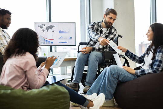 Multiracial group gathering with male wheelchair user sharing project papers during business discussion in office