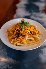 A plate of crispy French fries topped with seasoned beef, melted cheese sauce, diced tomatoes, cucumber, and fresh cilantro. The dish looks savory.