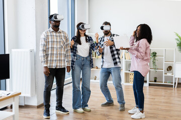 Diverse group of young adults, men and women, experiencing virtual reality headsets indoors while interacting and sharing fun moments together. The scene captures enjoyment, technology.