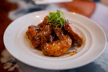 A plate of spicy glazed chicken wings garnished with sesame seeds and chopped green onion, served...