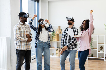 Group of multiethnic young adults participating in virtual reality activity with smiles. Colleagues showing teamwork and enjoying a tech-filled moment emphasizing innovation and shared experience.