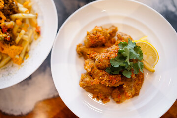 a crispy fried chicken wings topped with herbs and lemon slices, served on a white plate.