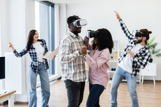 Diverse group of young men and women enjoying time using virtual reality glasses celebrating together indoors.