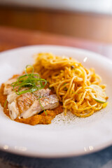 A serving of spaghetti next to grilled fish fillet, garnished with herbs and presented on tomato sauce, plated with a thin slice of lime for extra flavor.